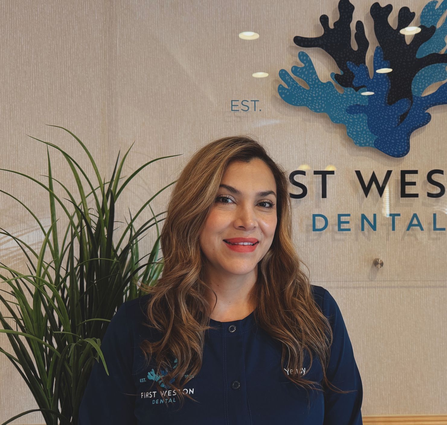 Woman in blue scrubs smiling in a dental office setting with 