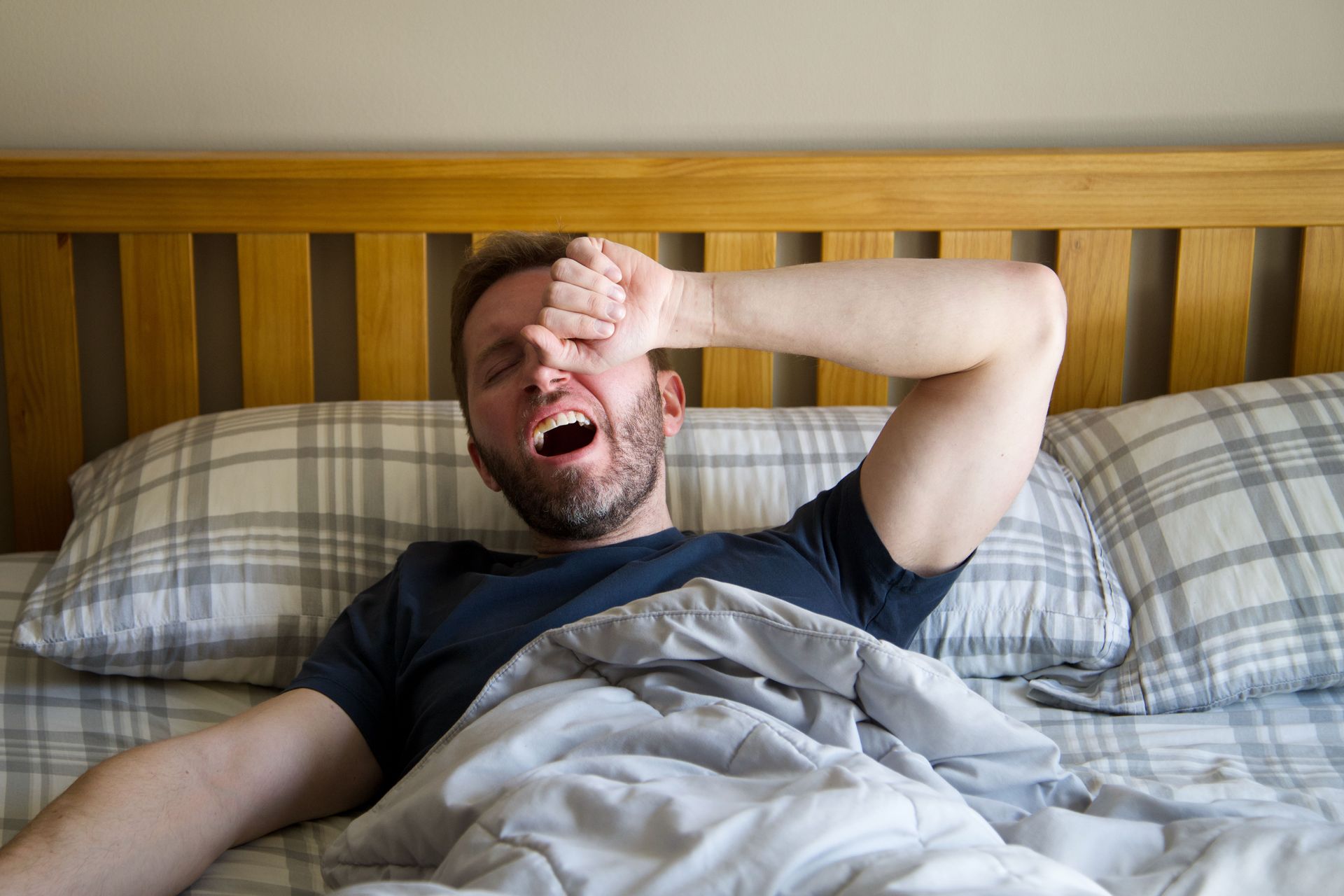 Man woken up in bed, rubbing eyes with hands indicating trouble sleeping