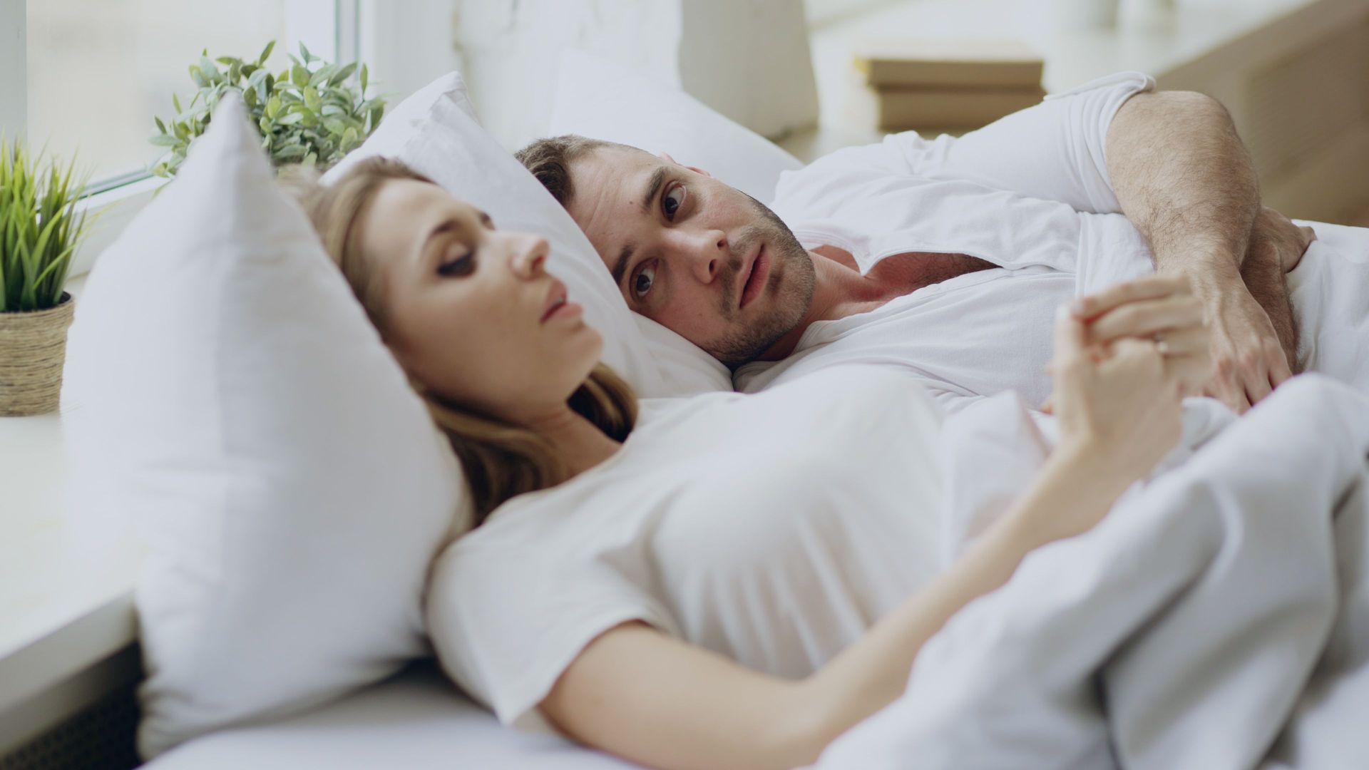 Man and woman laying bed with the man reaching over, looking concerned about the woman sleeping