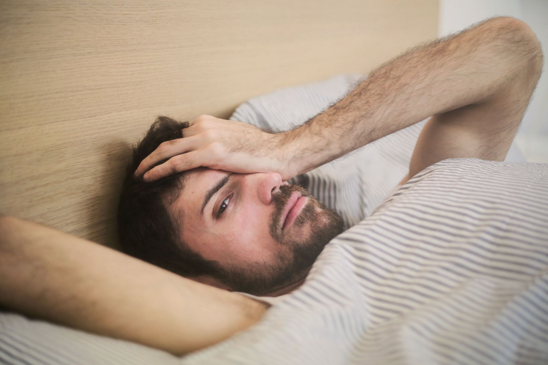 Man laying down in with hand on his head indicating difficulty sleeping