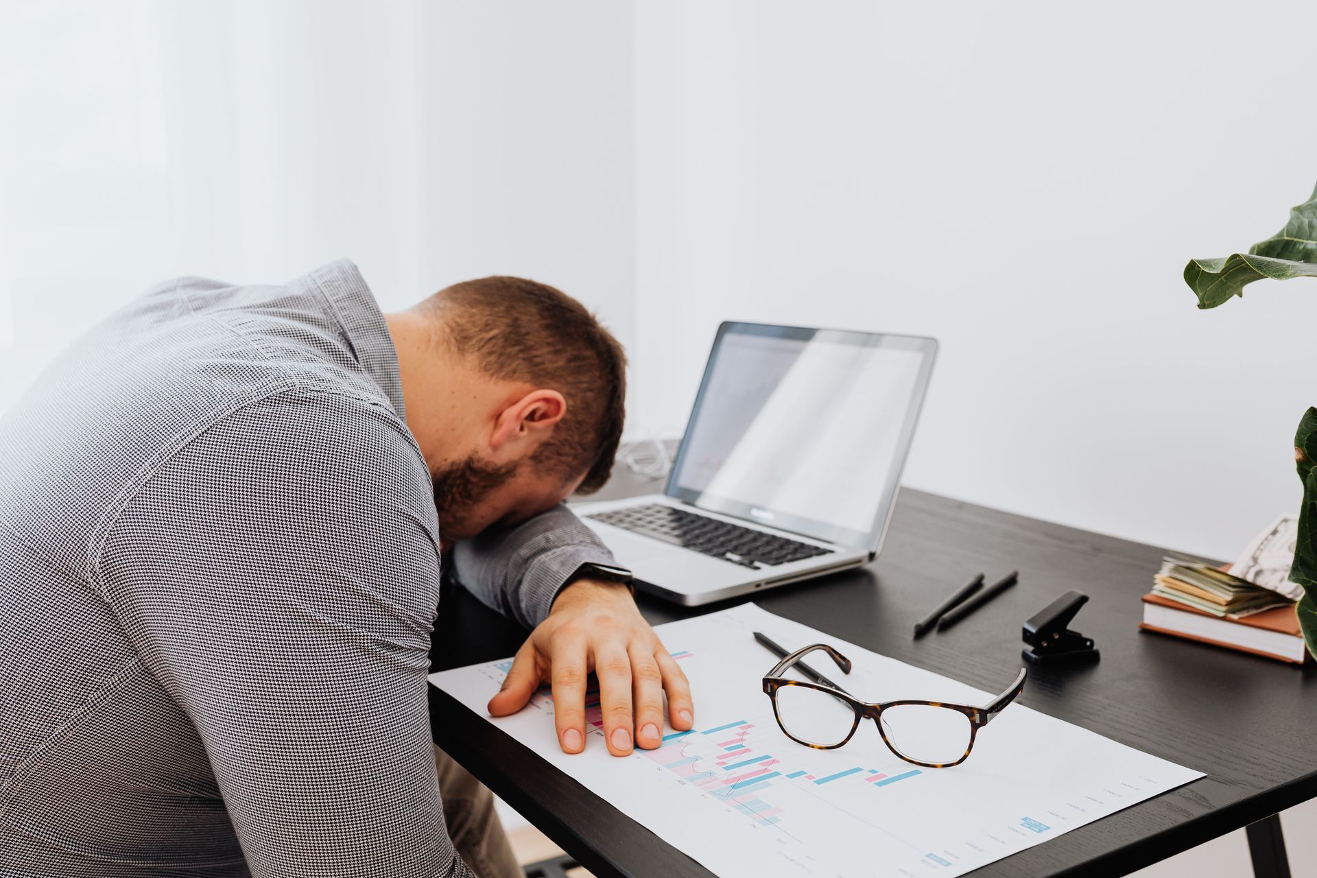 Man sitting down at a desk with his head resting on his arm, showing that he is tired