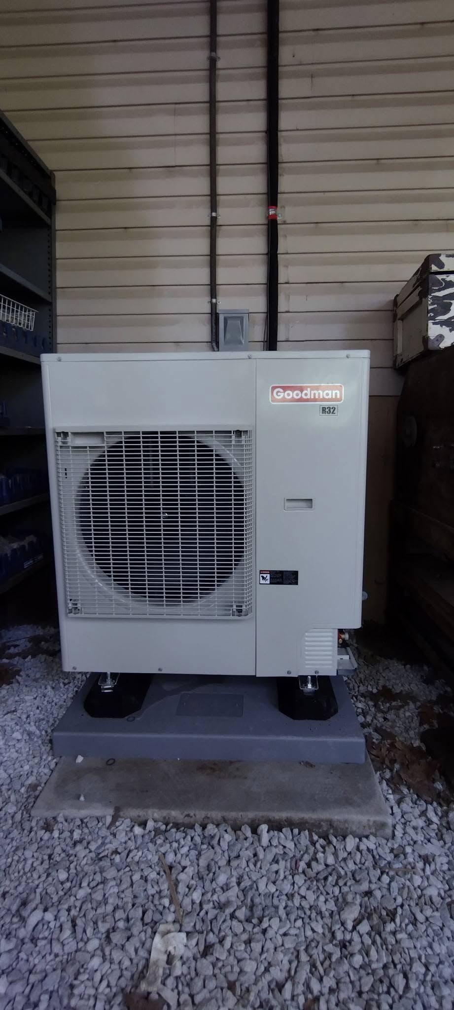 White outdoor HVAC unit on a concrete pad beside a building, with a large fan visible in front.