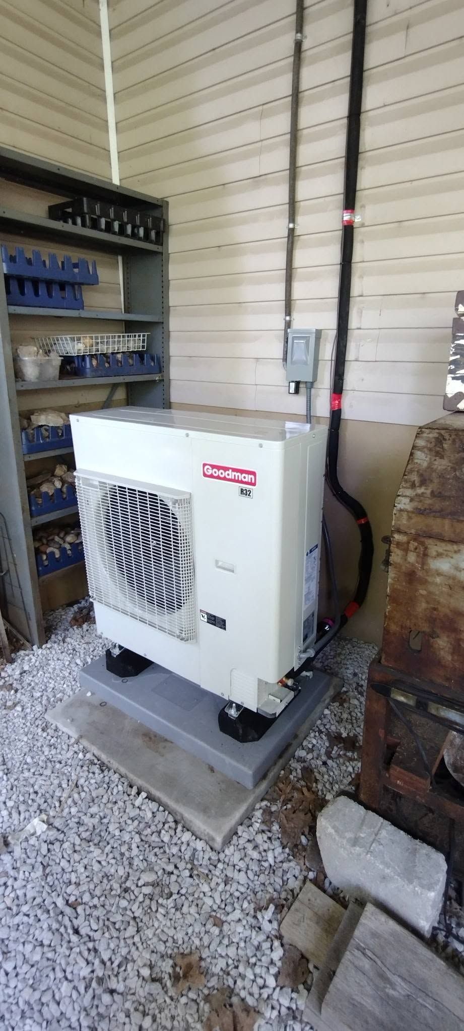 White outdoor HVAC unit on a gravel pad beside a building wall and stacked wood pallets