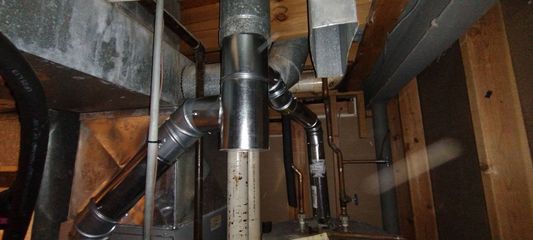 Crawlspace with exposed ductwork, pipes, and wooden framing in a dim utility area