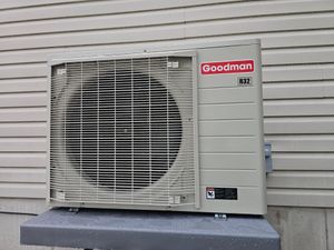 Goodman outdoor air conditioner unit beside a house with white siding