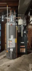 Tall black HVAC unit with silver ductwork in a basement utility area