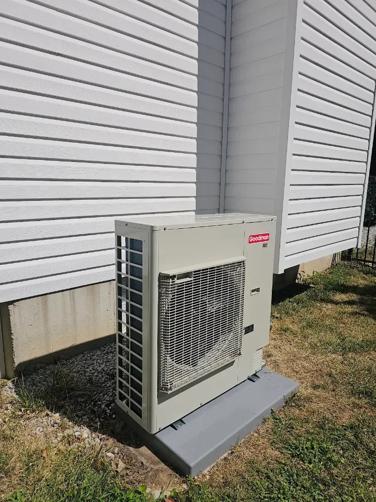Outdoor HVAC unit beside a white building wall on a concrete pad.