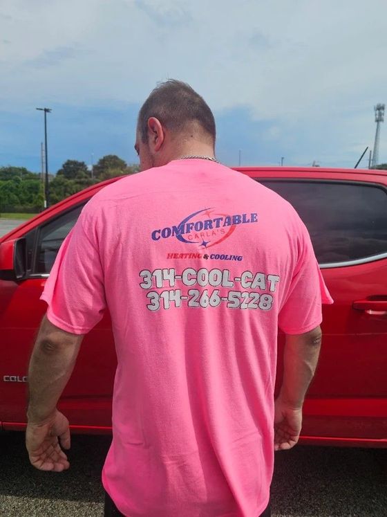 Person in a bright pink T-shirt stands beside a red car outdoors, showing a company logo and phone number.