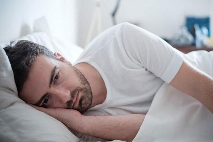 Un hombre está acostado en la cama con la cabeza sobre una almohada.