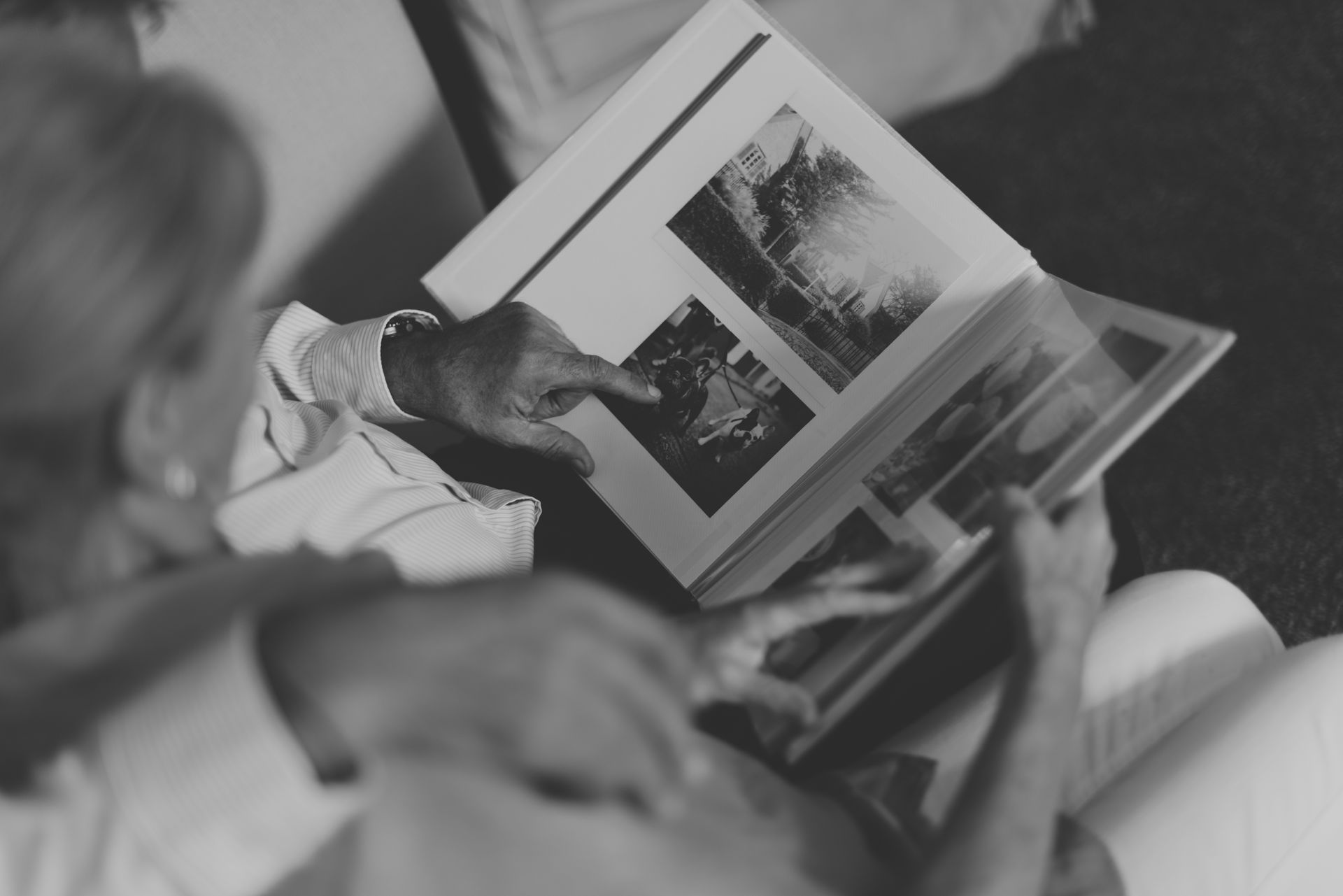 Two people looking at a photo album, with one person pointing at a black-and-white photograph.
