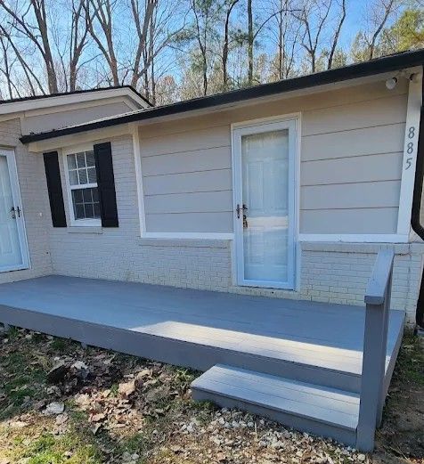 A house exterior with a freshly painted gray wooden deck and a single step leading up to a light-colored door.