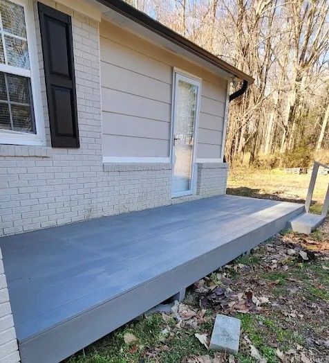 A newly built gray deck attached to the side of a house with light-colored brick and siding, set against a wooded backdrop.
