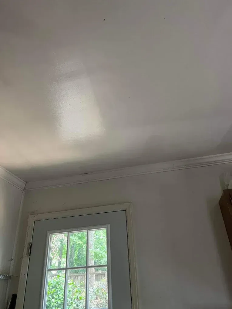 A white ceiling with a rectangular patch of light above a door frame with white molding and a glass pane window.