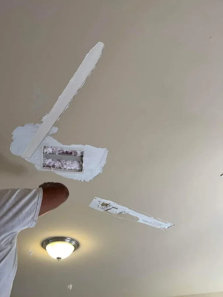 A person patches drywall repairs on a beige ceiling near a light fixture.