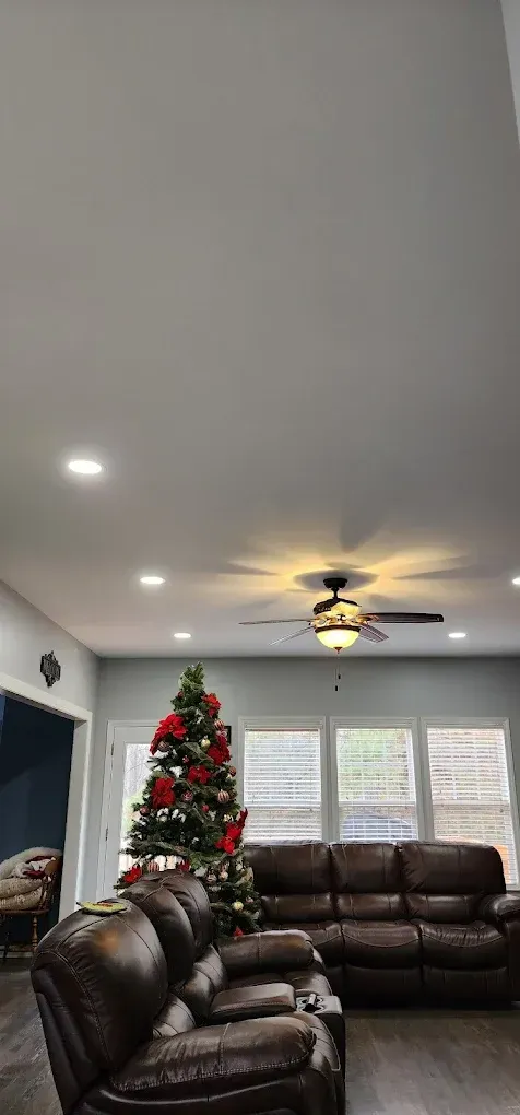 A living room with two brown leather couches, a decorated Christmas tree, and a ceiling fan with lights.