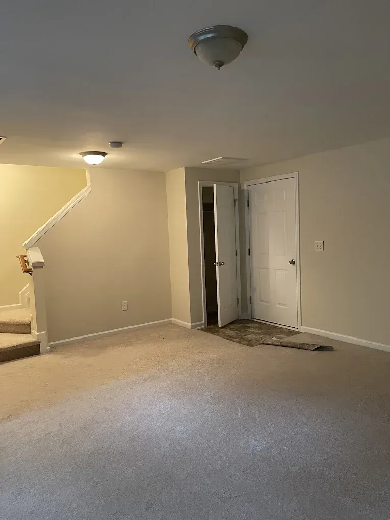 A carpeted room with beige walls, a staircase on the left, and a white door leading to a closet on the right.