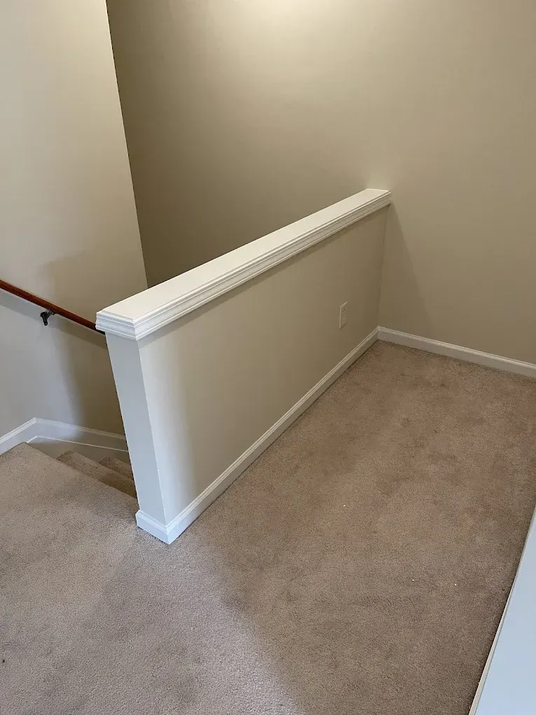 A carpeted stair landing with a short half-wall featuring white decorative molding and a wooden handrail on the left.