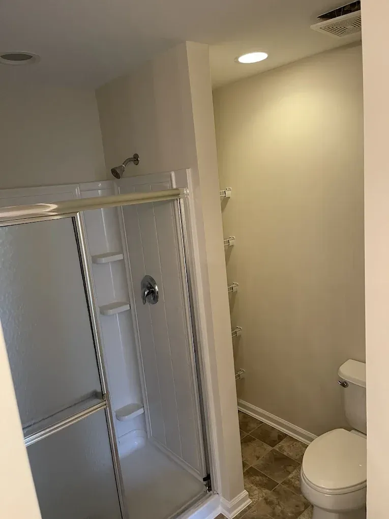 A bathroom featuring a glass shower stall on the left and a white toilet on the right, set against light-colored walls.