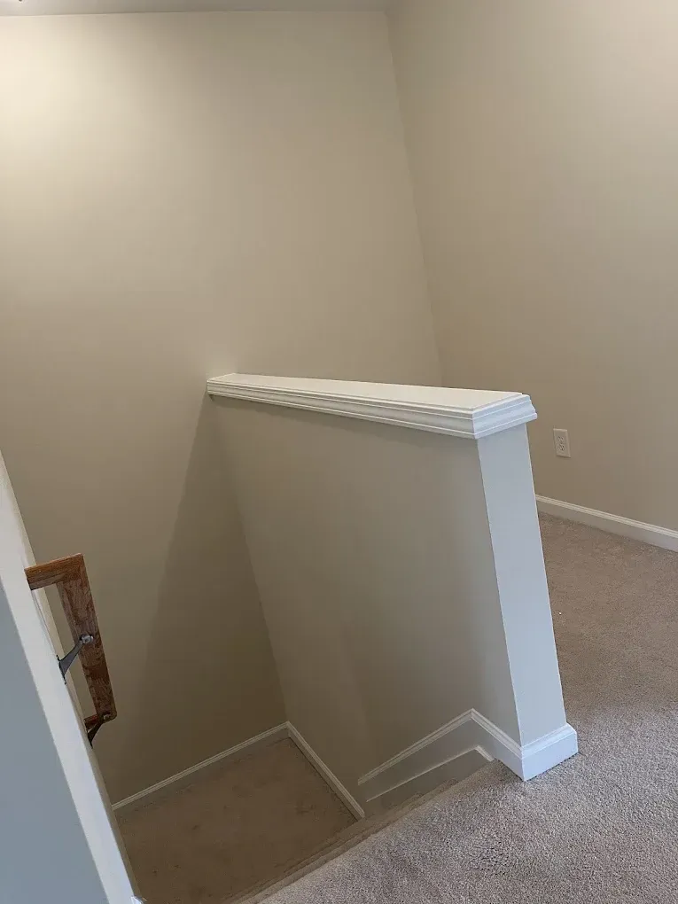 A staircase viewed from above, featuring beige walls, carpeted stairs and flooring, and a white half-wall with molding.