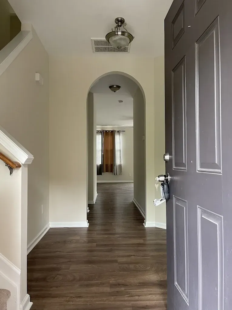 A view from an open, dark gray front door into a neutral-toned hallway with wood-style flooring and an arched entryway.