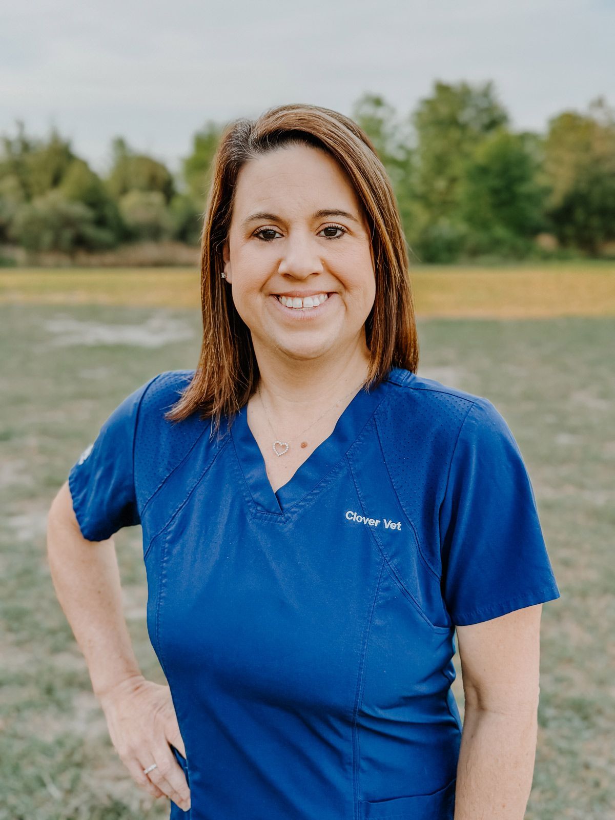 A woman in a blue scrub top is standing in a field.