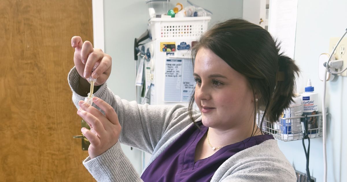 Elisabeth in a purple scrub, is holding a syringe in her hand.