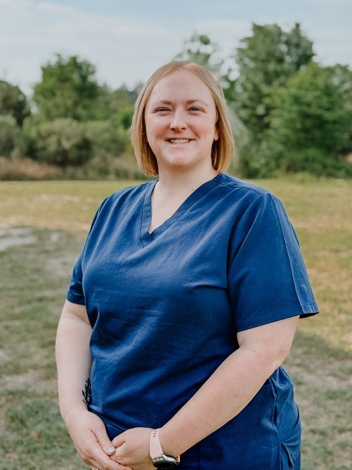 A woman in a blue scrub top is standing in a field.