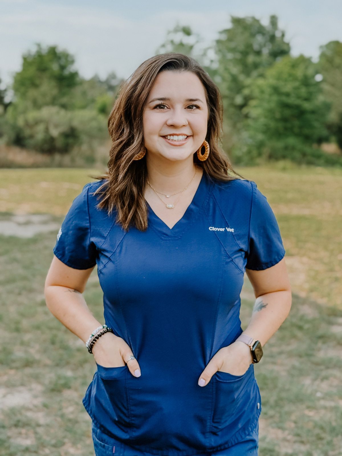 A woman in a blue scrub top is standing in a field.