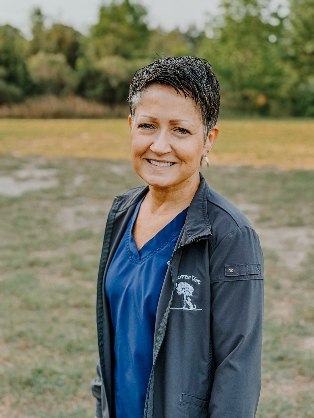 A woman in a blue scrub top is standing in a field.