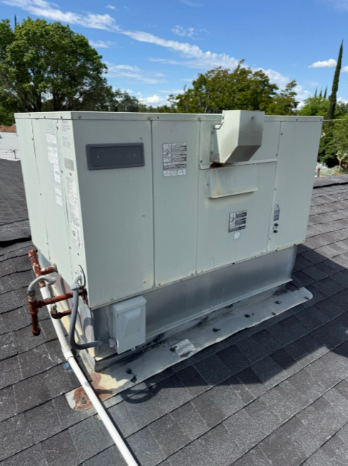 Large white rooftop HVAC unit on a shingled roof under a blue sky