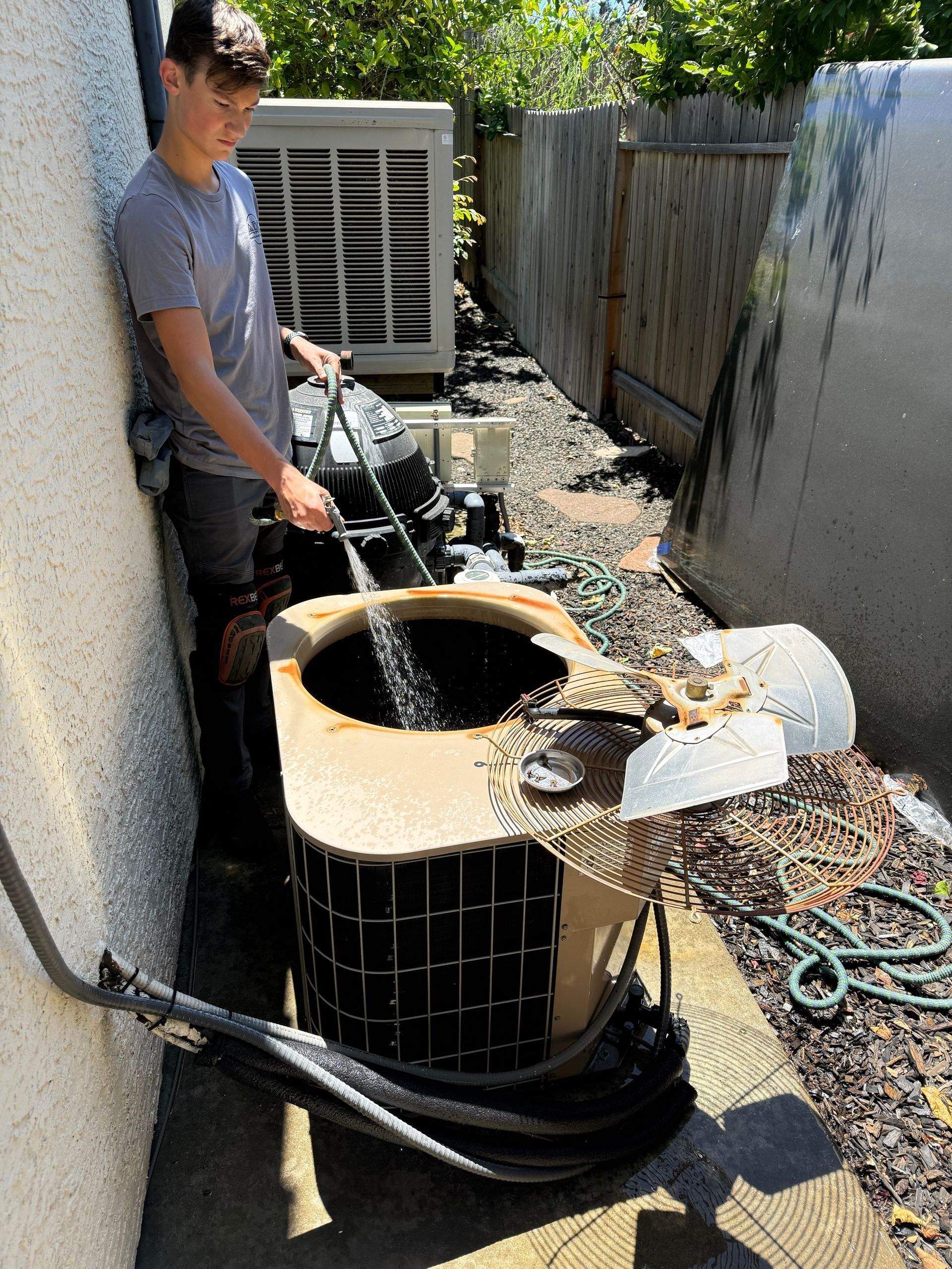 Person pouring water into an outdoor air conditioning unit in a narrow side yard