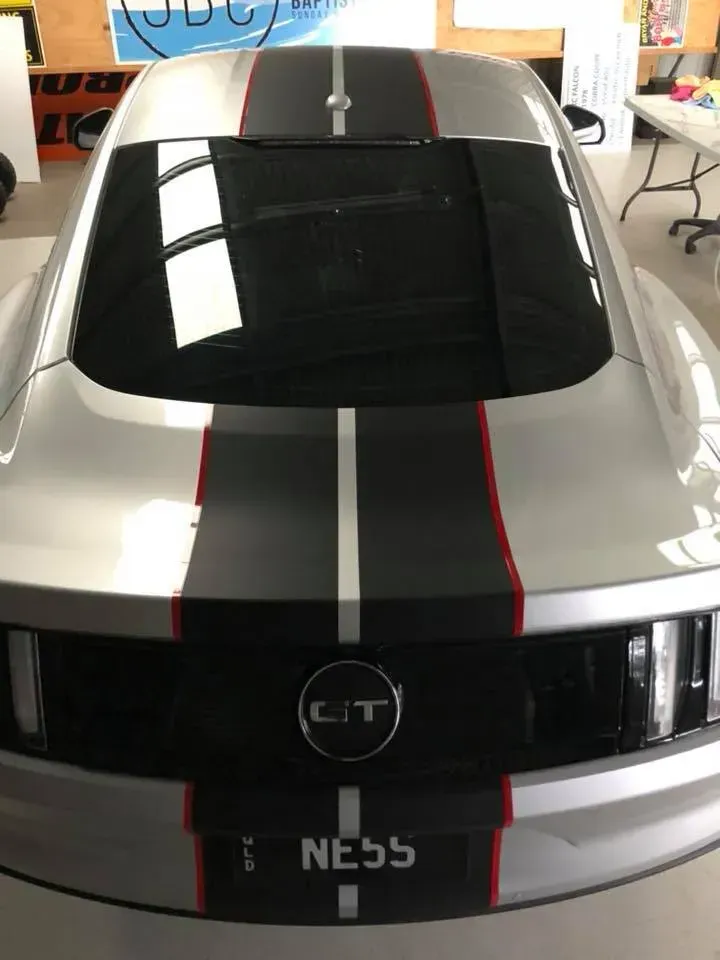 A silver mustang with black and red stripes is parked in a garage.