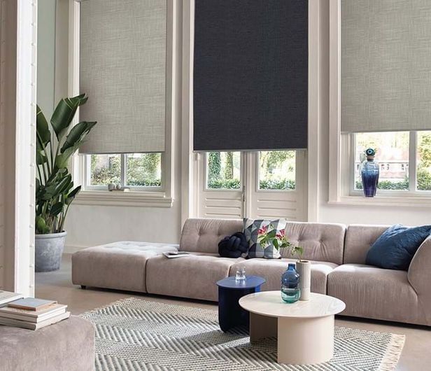 Living room with neutral sectional sofa, round coffee tables, window blinds, and large potted plant. Living room with neutral sectional sofa, round coffee tables, window blinds, and large potted plant.
