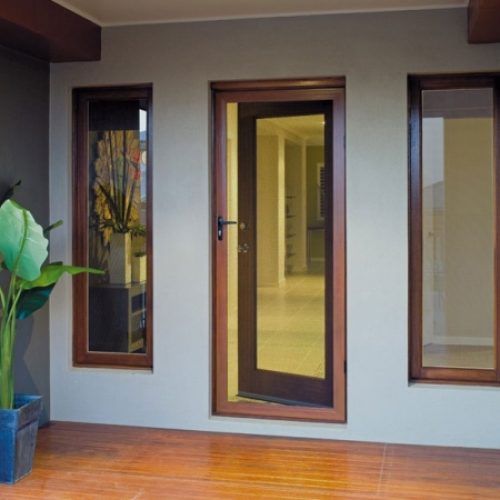 Wooden door and windows on a light gray wall with a wooden floor. A green plant is to the left. Wooden door and windows on a light gray wall with a wooden floor. A green plant is to the left.