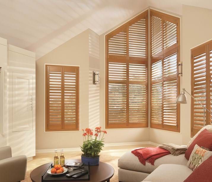 Living room with wooden shutters on various windows, including a large triangular window, soft lighting. Living room with wooden shutters on various windows, including a large triangular window, soft lighting.