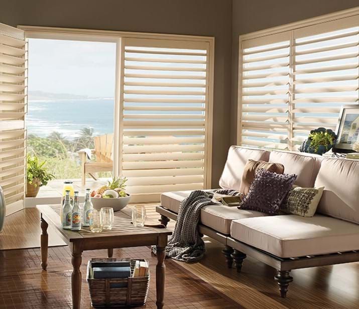 Living room with wooden shutters, a view of the ocean, a beige sofa, and a wooden coffee table. Living room with wooden shutters, a view of the ocean, a beige sofa, and a wooden coffee table.