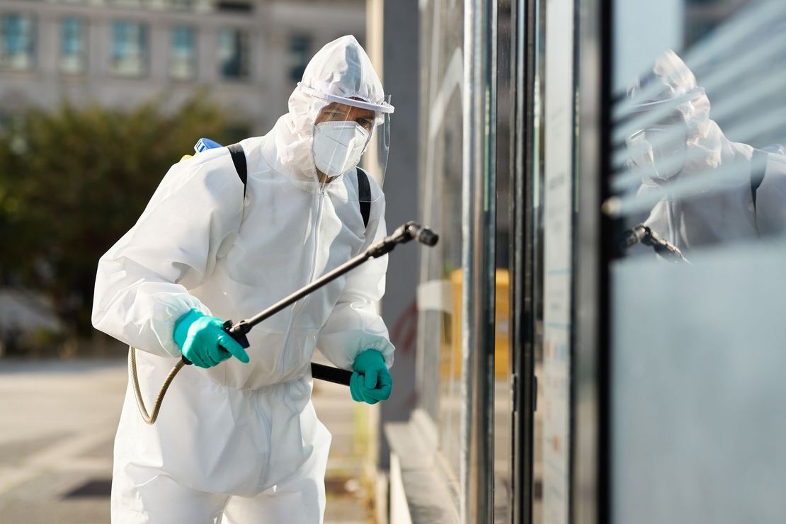 A man in a protective suit is spraying a window with a sprayer.