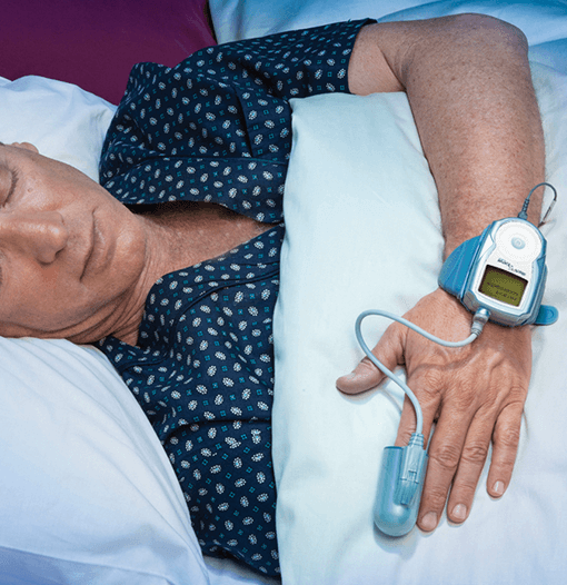 Paciente em repouso na cama, com um oxímetro de pulso no dedo e um monitor de pressão arterial no pulso