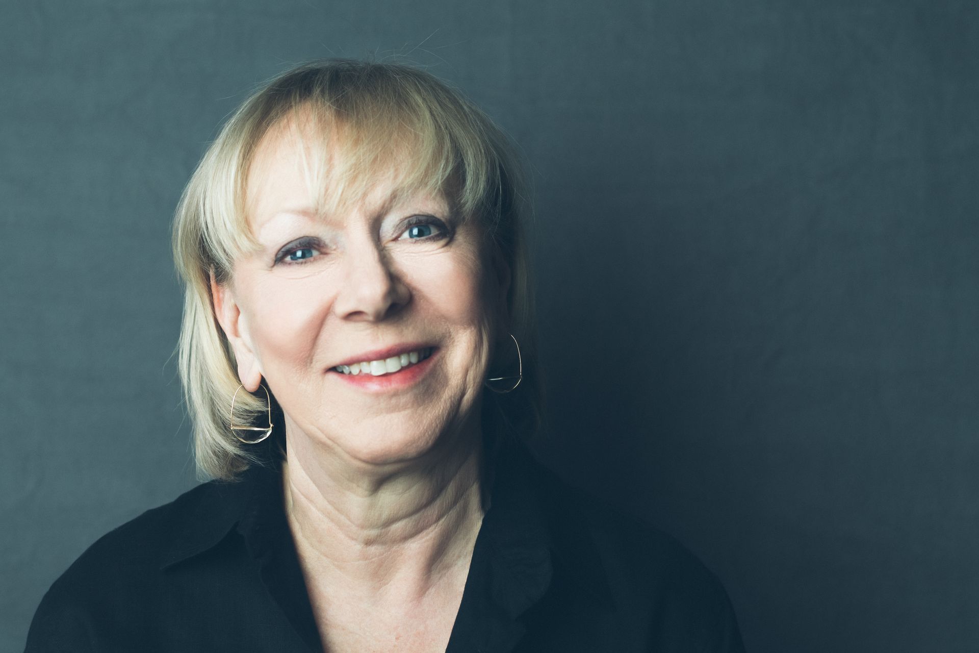 A woman with blonde hair and earrings is smiling for the camera.