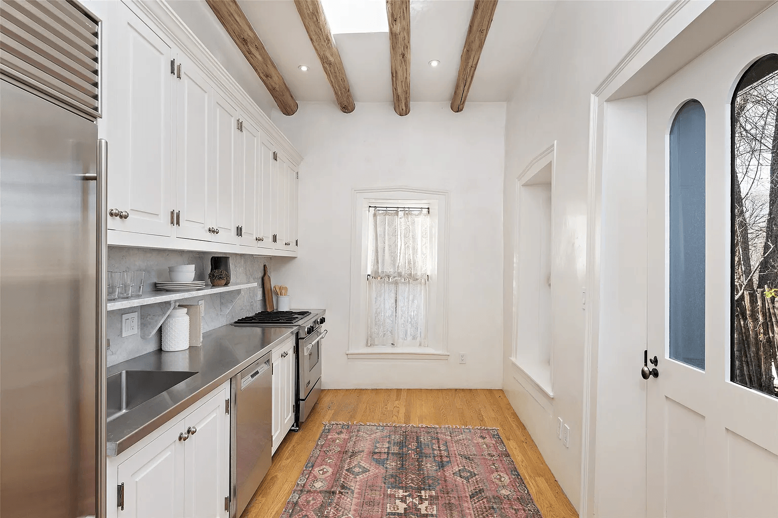 A kitchen with white cabinets , stainless steel appliances , a rug and wooden beams.