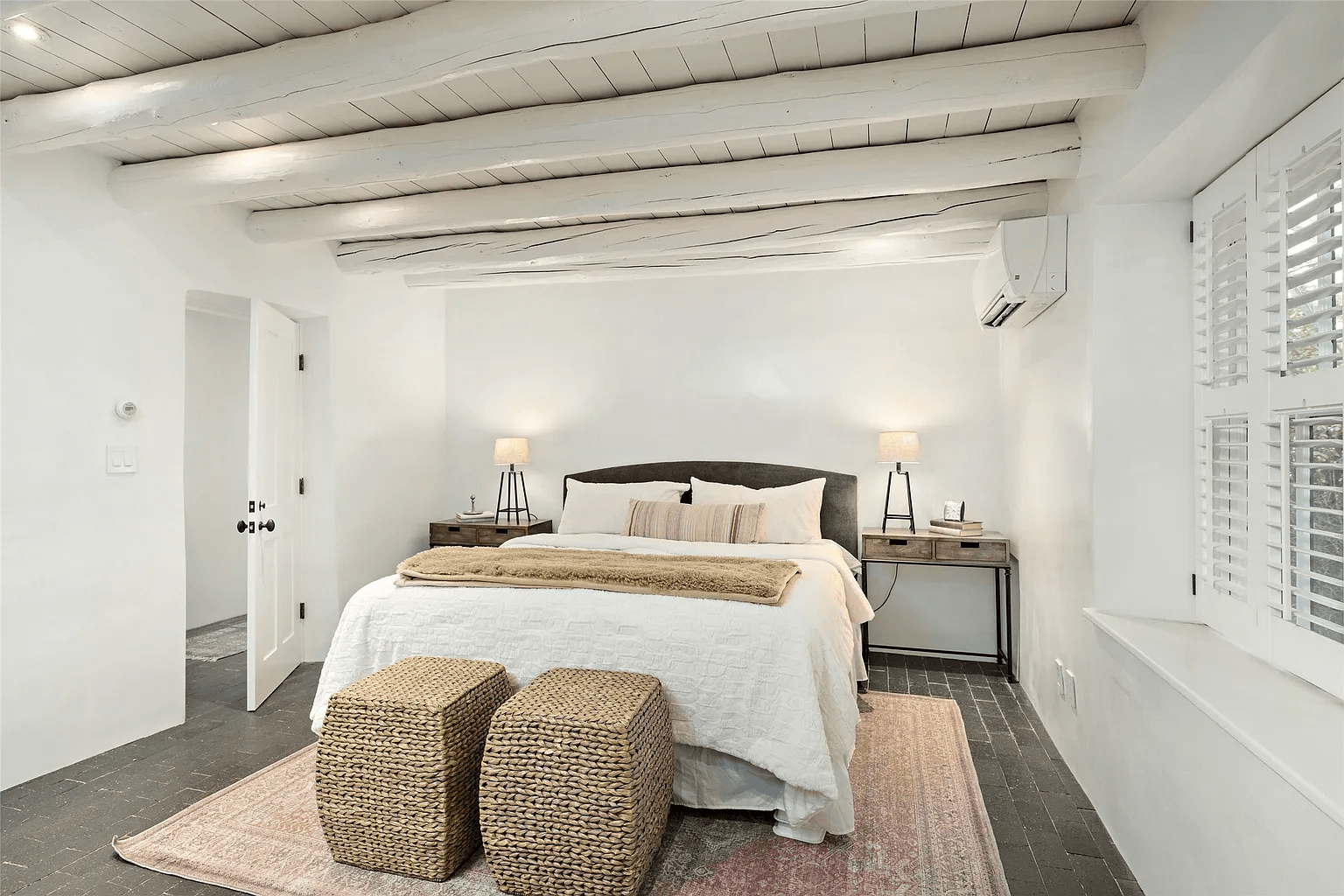 A bedroom with a bed and two wicker ottomans.