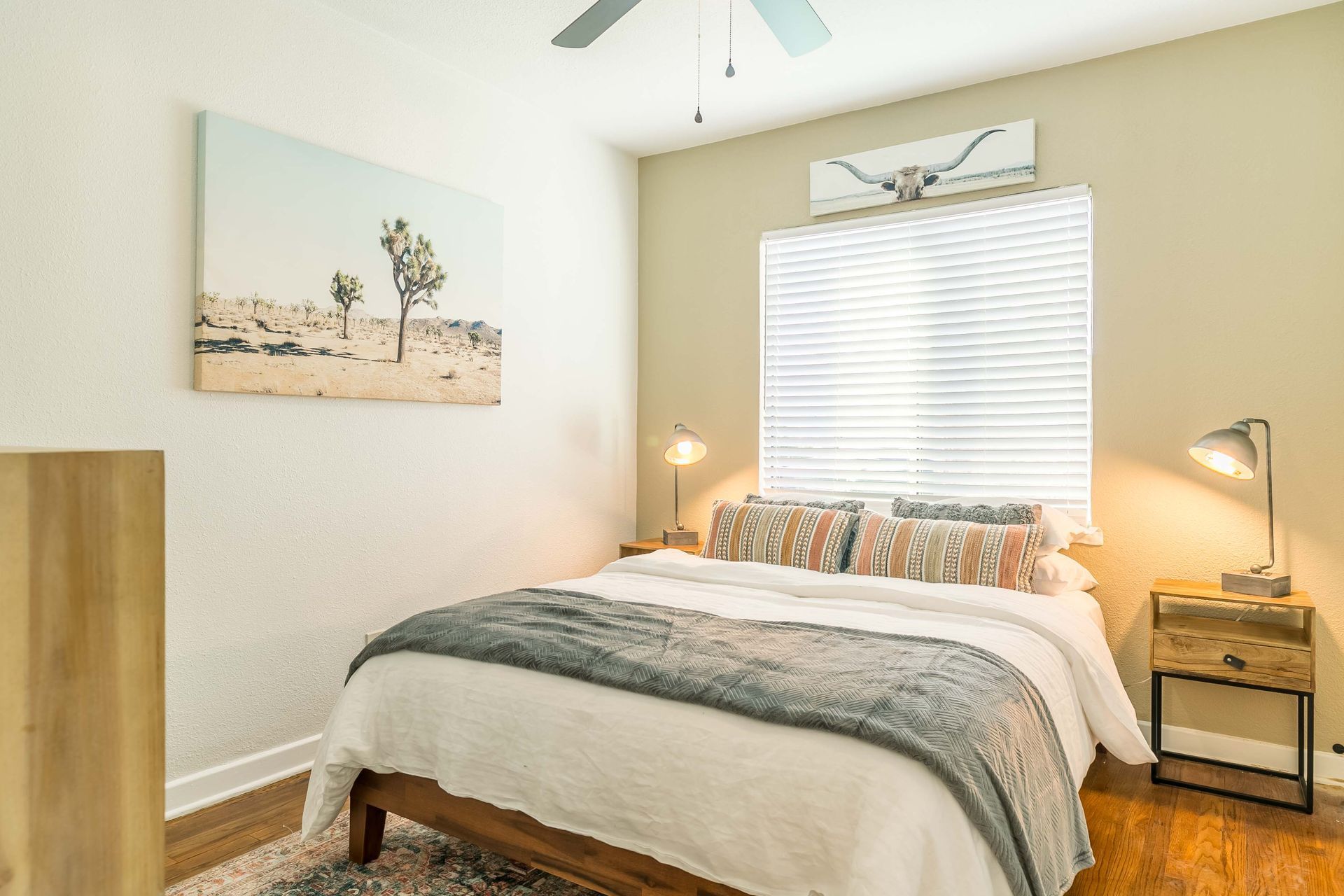 A bedroom with a bed , nightstands , a painting on the wall and a ceiling fan.