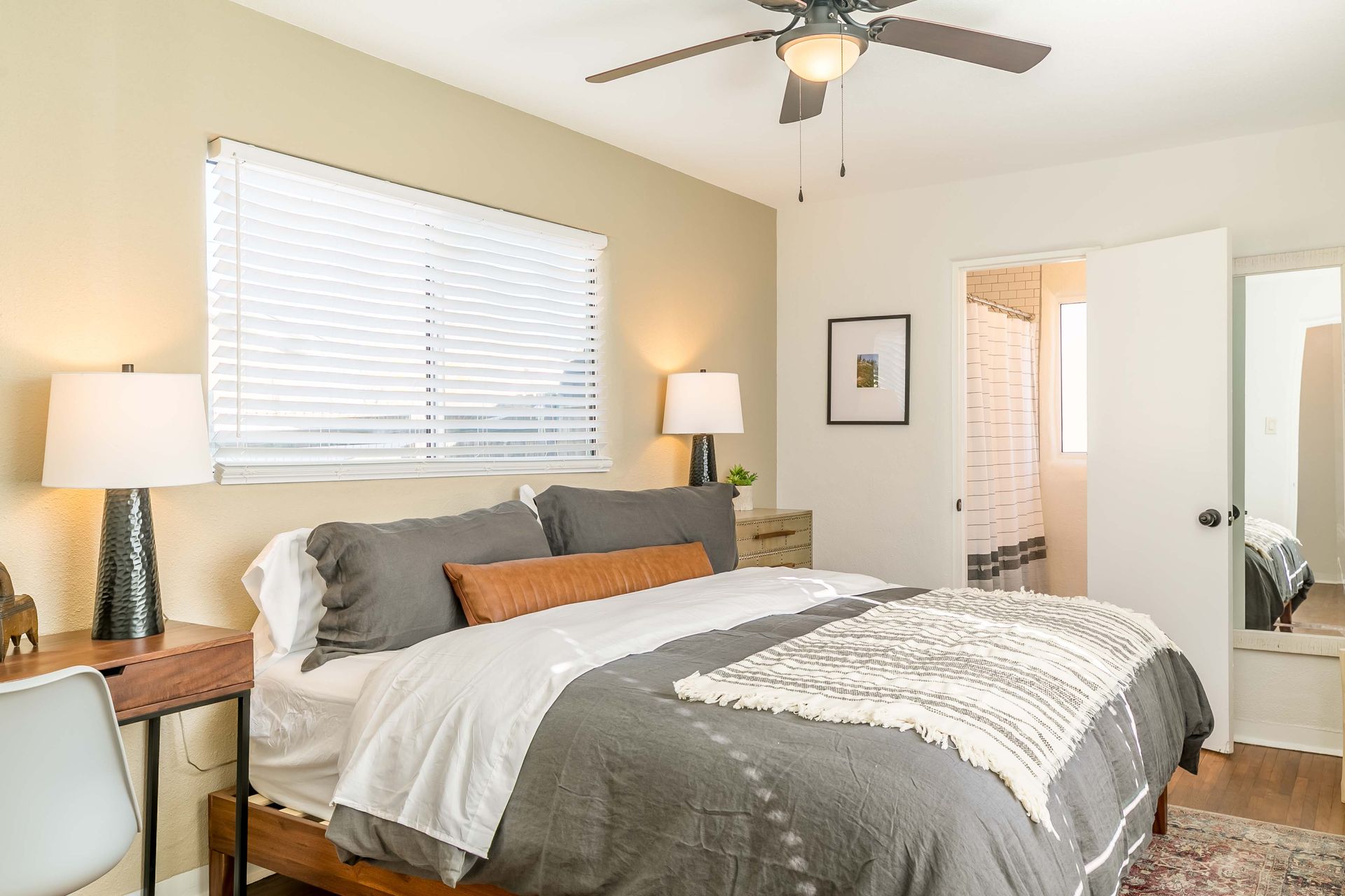 A bedroom with a bed , desk , lamps and a ceiling fan.