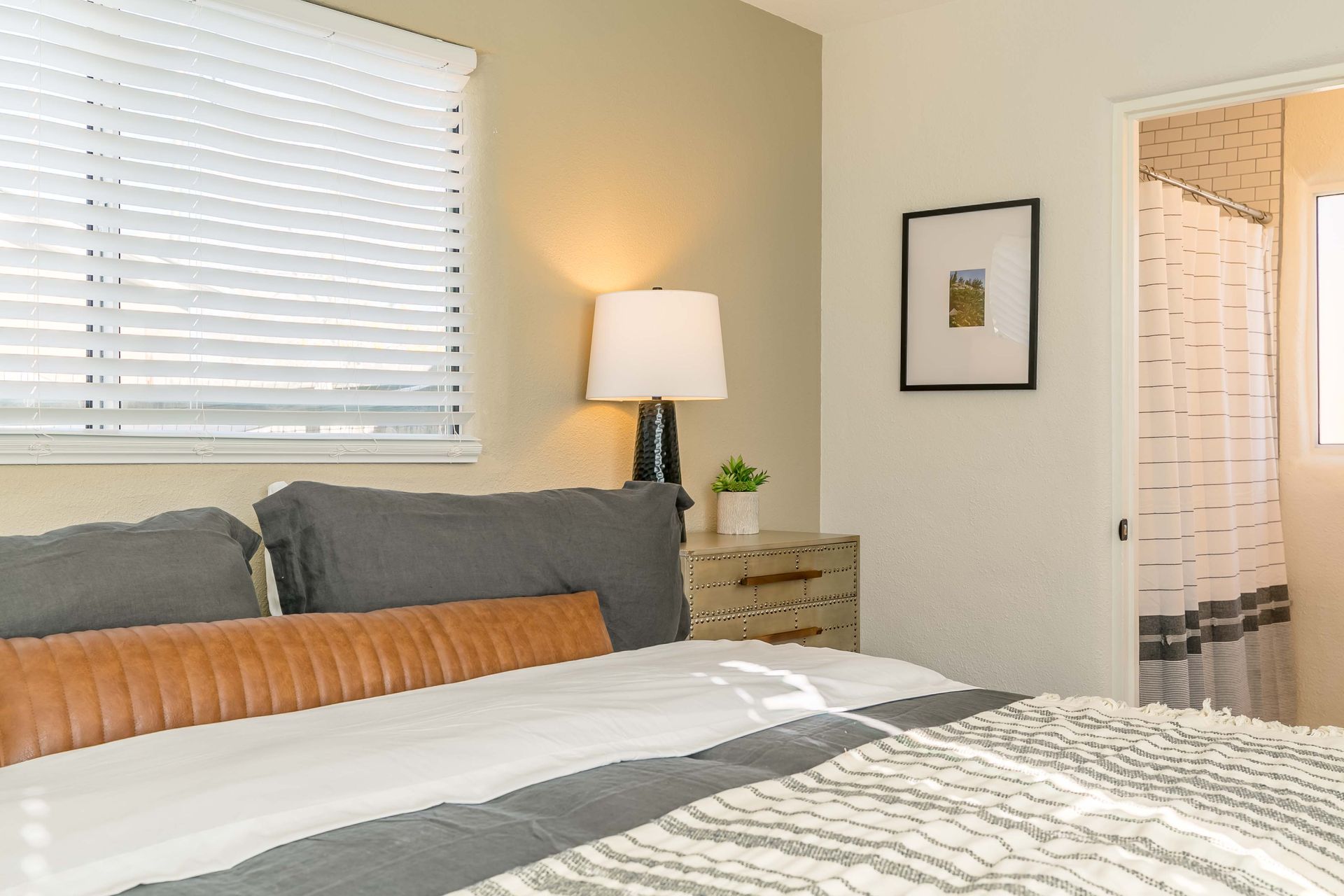 A bedroom with a bed , nightstand , lamp and window.