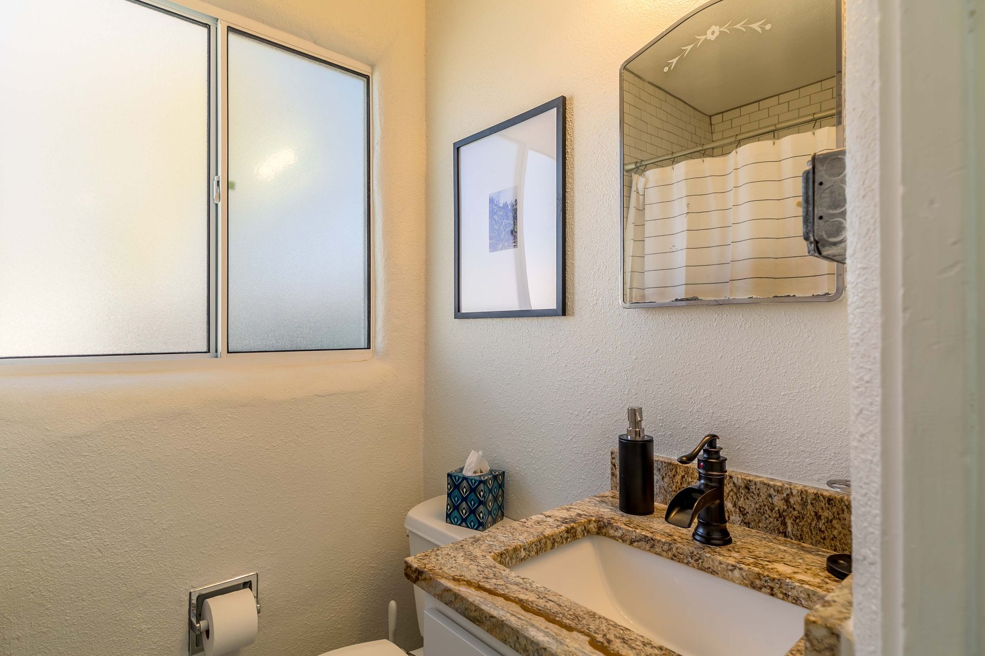 A bathroom with a toilet , sink , mirror and window.