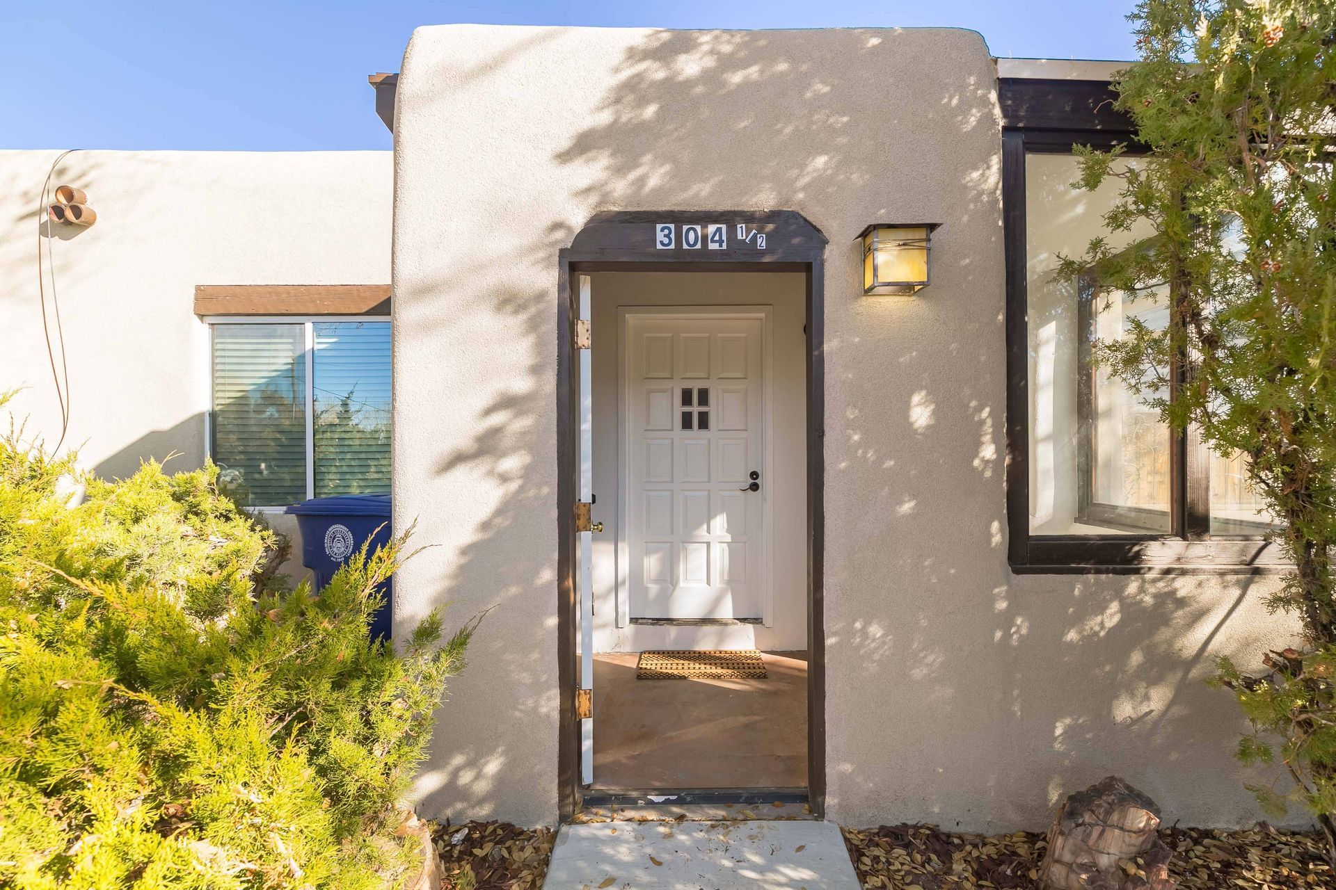 A house with a white door and a blue trash can in front of it.