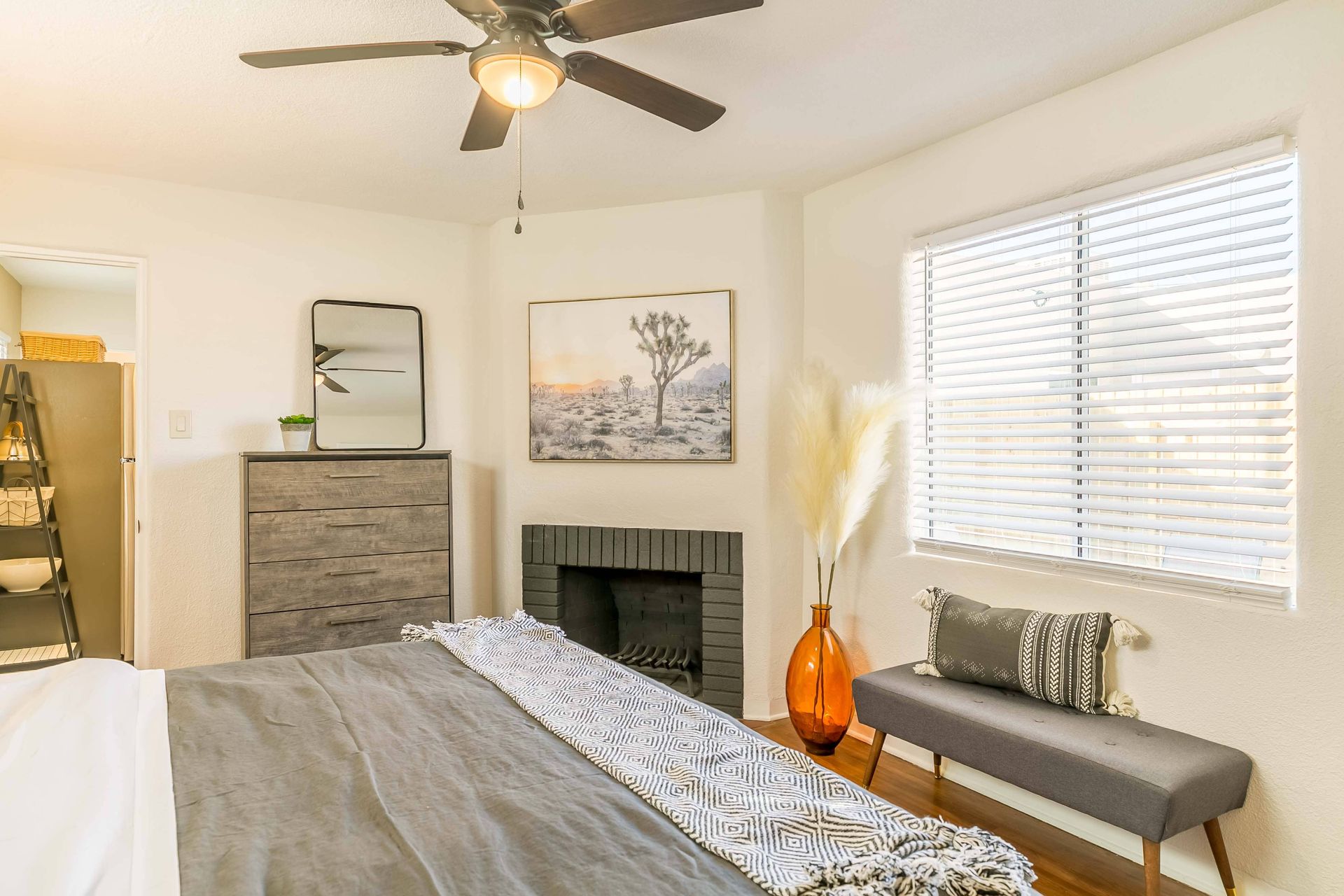 A bedroom with a bed , dresser , fireplace and ceiling fan.