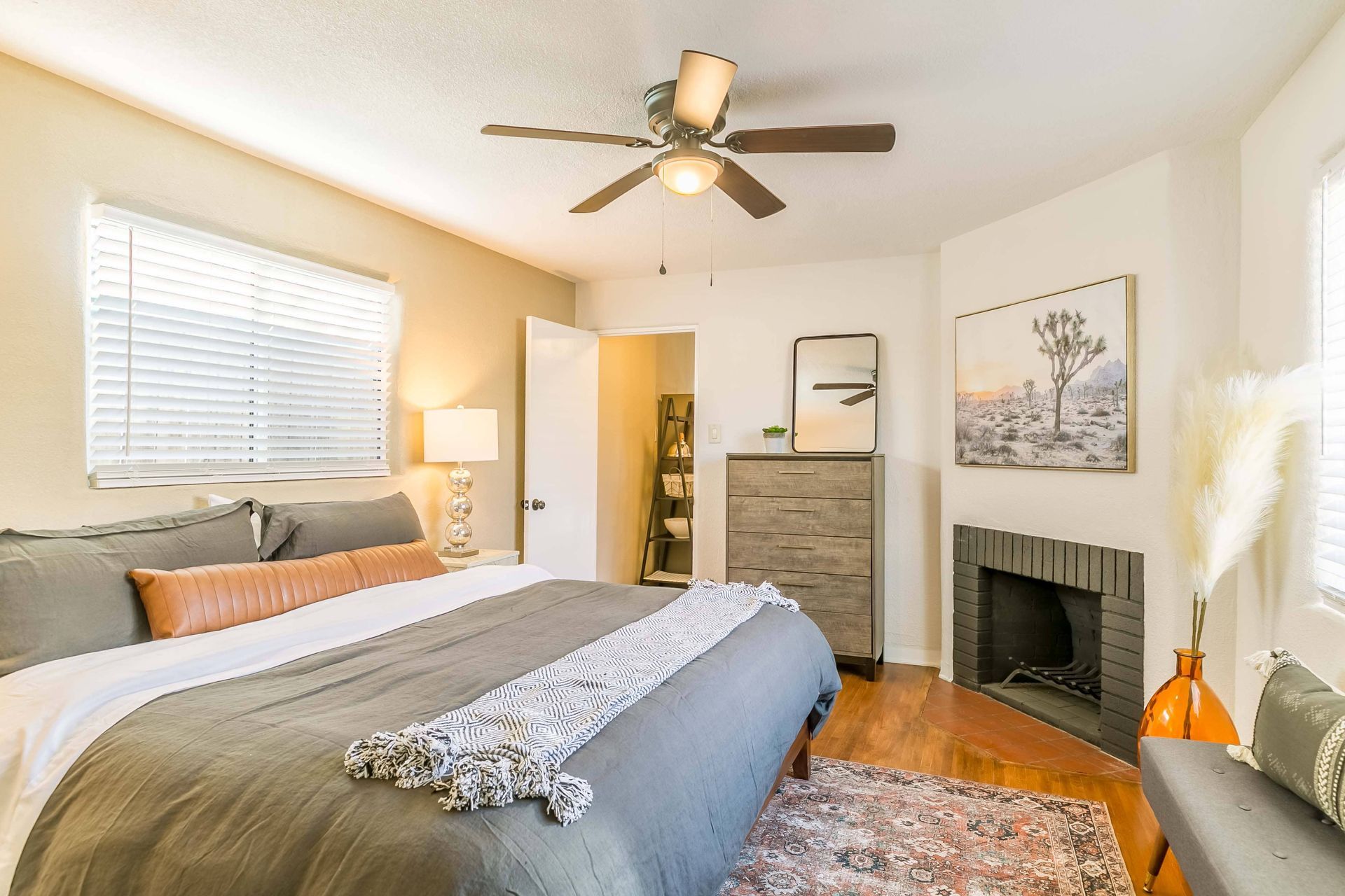 A bedroom with a king size bed , fireplace , dresser and ceiling fan.