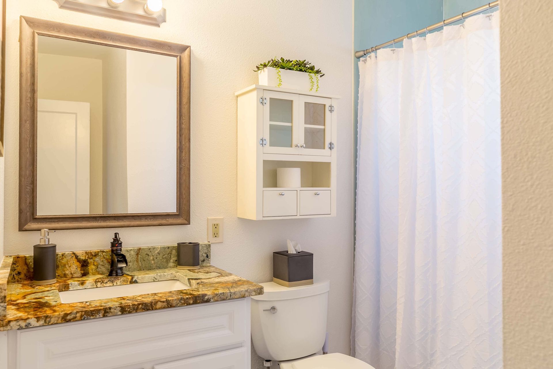 A bathroom with a toilet , sink , mirror and shower curtain.