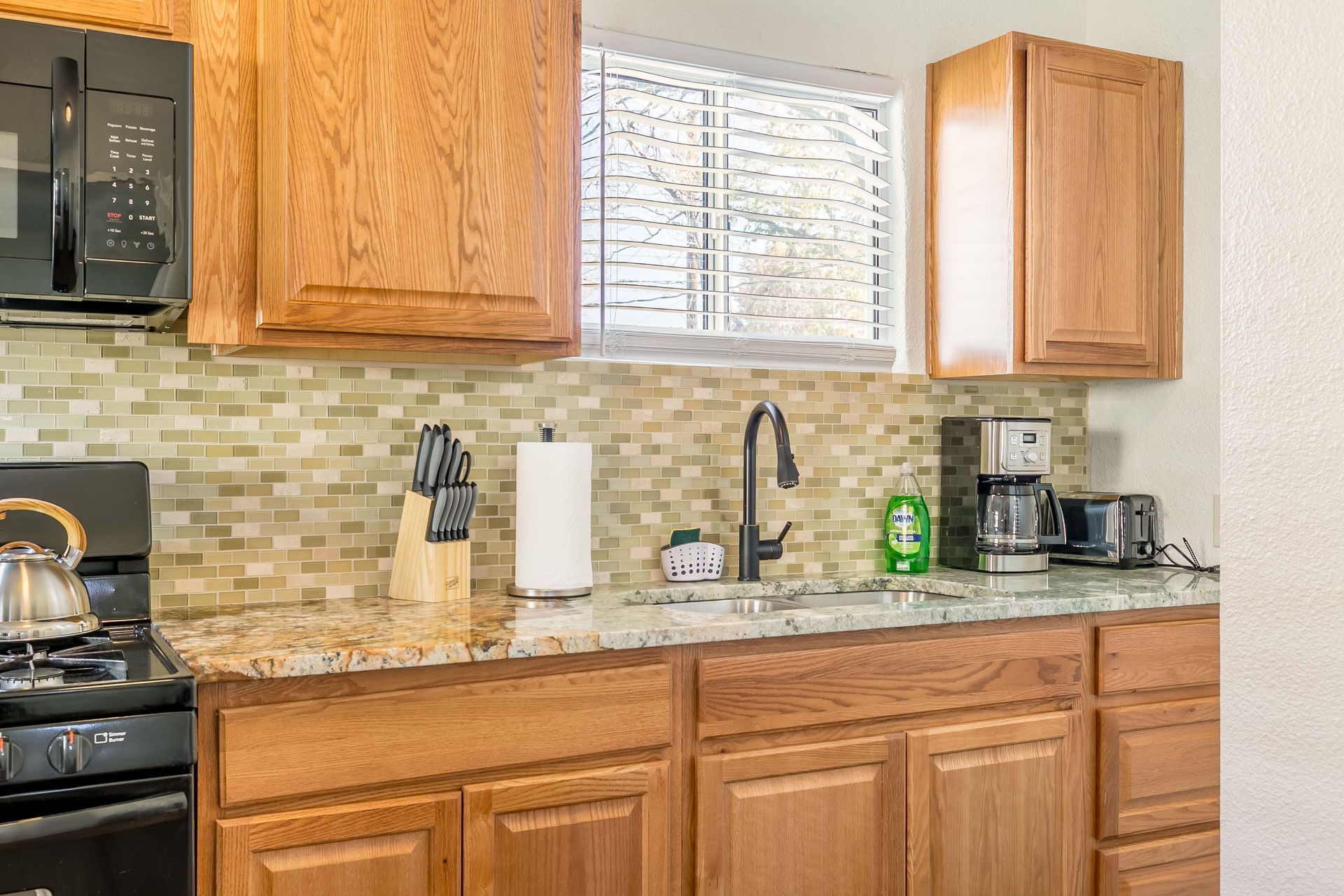 A kitchen with wooden cabinets , granite counter tops , a stove and a microwave.